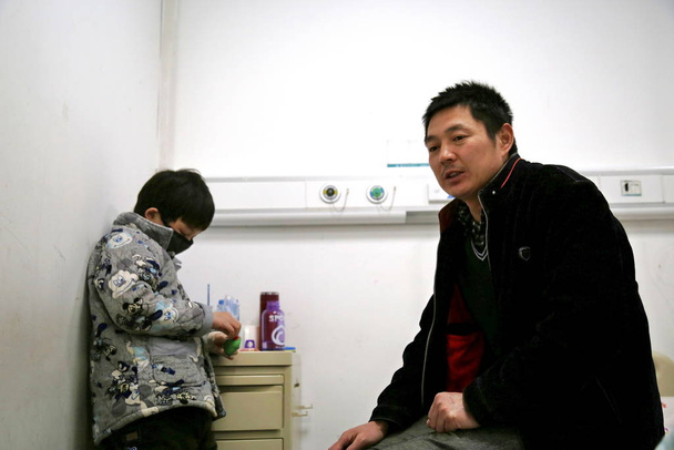 Chen Yuntao, right, who wore a horse head mask and offered to give pedestrians a ride for five yuan ($1) to collect money for his sick son's leukemia treatment, looks worried as he sits next to his son in a ward at a tumour hospital in Hefei city, ea - Fotoğraf, Görsel