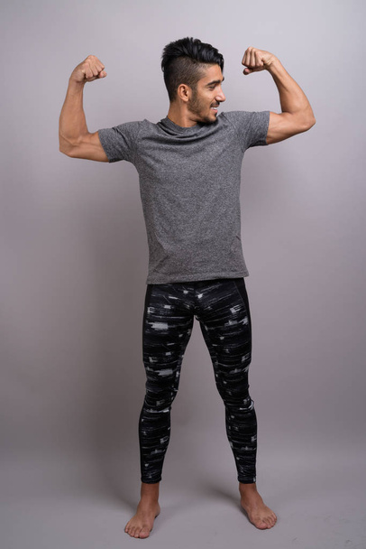 Young handsome Persian man ready for gym against gray background - Foto, imagen