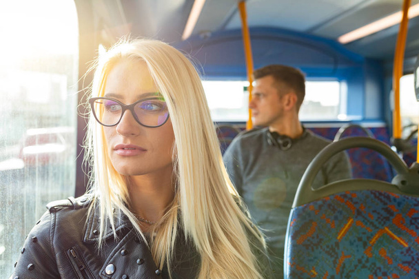 Woman and man travelling by bus in London. Beautiful blonde woman looking out of the window with sun comingh through, man on background. Lifestyle and travel concepts - Zdjęcie, obraz