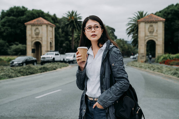 молодая женщина профессор собирается работать утром в университет в Стэнфорде Пало-Альто Калифорния США азиатская женщина преподает китайский в школе держа чашку кофе нести рюкзак ходить по дороге
. - Фото, изображение