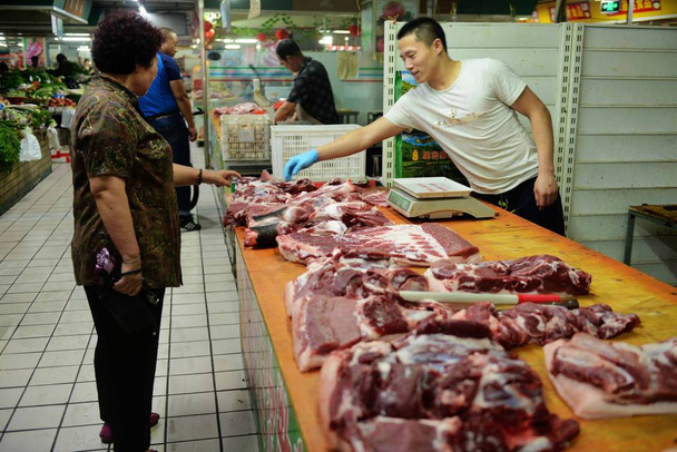 A customer shops for pork at a wet market in Qingdao city, east China's Shandong province, 9 July 2015.  - Foto, Imagen