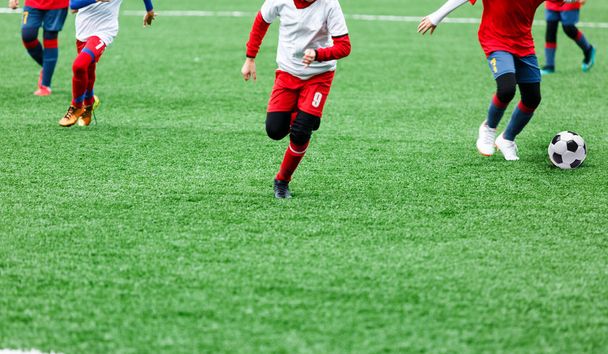 Los chicos en ropa deportiva roja y blanca juegan fútbol en el campo de hierba verde. Juego de fútbol juvenil. Niños deporte competición, niños juega al aire libre, actividades, entrenamiento
 - Foto, imagen