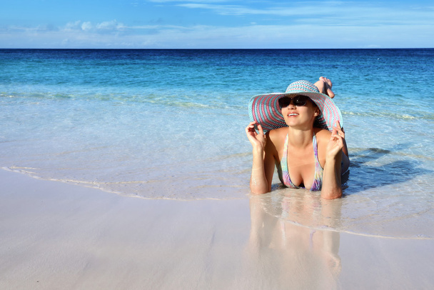 Happy girl in a Panama hat and sunglasses lying on the beach - Photo, Image