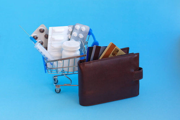 Ένα καλάθι με χάπια, καθώς και συρίγγων δίπλα σε ένα πορτοφόλι με πιστωτικές κάρτες σε μπλε φόντο - Φωτογραφία, εικόνα