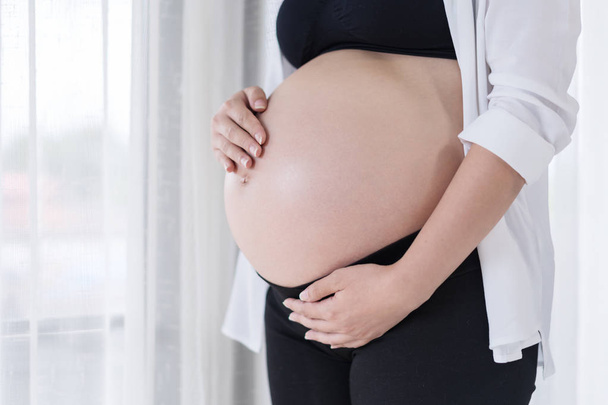 Detailní záběr břicho těhotné ženy s pozadí okna - Fotografie, Obrázek