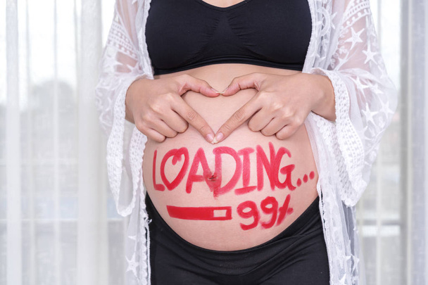 妊娠中の女性の塗装ブラシの単語 - 彼女の腹に 99% の読み込みと心臓の形で手をつないで - 写真・画像