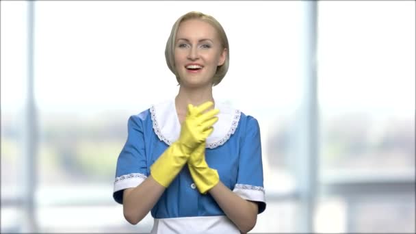 attraktives Zimmermädchen auf verschwommenem Hintergrund. Die schöne Hausfrau in gelben Handschuhen lächelt und blickt in die Kamera. verschwommener Fensterhintergrund. - Filmmaterial, Video