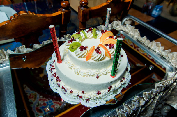 Doppelstocktorte in weiß. Süßgebäck. Kuchen mit Orangen und Kiwi verziert. Kerzen-Feuerwerk auf dem Kuchen. Dessert. Buttercreme. Keks. - Foto, Bild