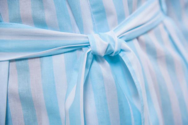 Cotton bathrobe. Textile. Bathrobe light blue with white stripes. The texture of the fabric. Cotton. Robe belt People. Clothes for hotels and hotels. Woman. Blonde hair. Arm. - Photo, Image