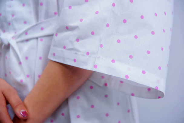 Cotton bathrobe. Textile. White robe with a pink polka dot print. The texture of the fabric. Cotton. Robe belt People. Clothes for hotels and hotels. Woman. Arm. - Photo, Image