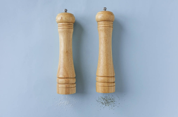 Set houten peper en zout slijpmachines of molens liggen aan hun zijden op een blauwe achtergrond met laterale kopie ruimte - Foto, afbeelding