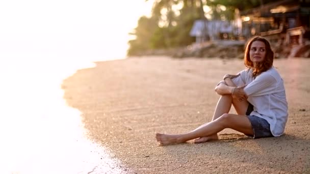 Młoda, piękna kobieta, znajduje się przy piaszczystej plaży i spogląda w dal. Szczęśliwa dziewczyna siedzi nad morzem czeka na swojego chłopaka. - Materiał filmowy, wideo