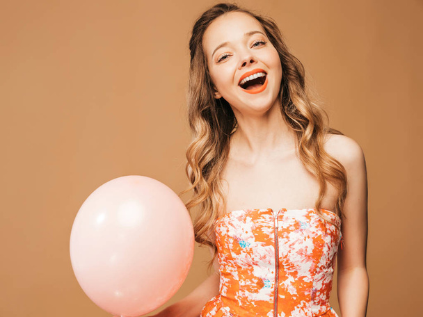 Portrait of excited young girl posing in trendy summer colorful dress. Smiling woman with pink air balloon posing on golden background. Model ready for party - Fotografie, Obrázek