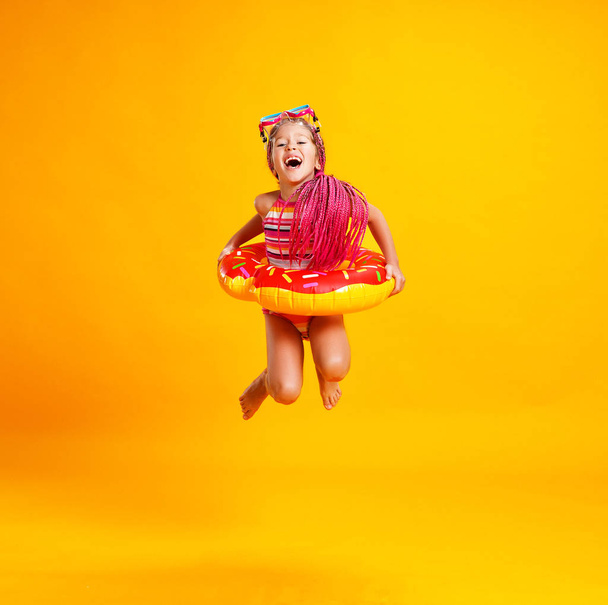 boldog gyermek lány fürdőruha úszás fánk gyűrű egy sárga színű háttér mintázata - Fotó, kép