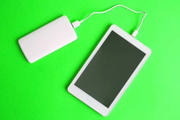 Flat lay of blank screen digital tablet device charging with power bank on green background minimal creative concept. Space for copy. - Foto, imagen