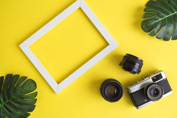 Flat lay of retro photo camera with lenses, photo frame and monstera leaves against yellow background minimal creative tropical concept. - Photo, Image