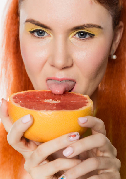 Young redhead woman licks a grapefruit on a white background. concept of healthy eating - Foto, Bild