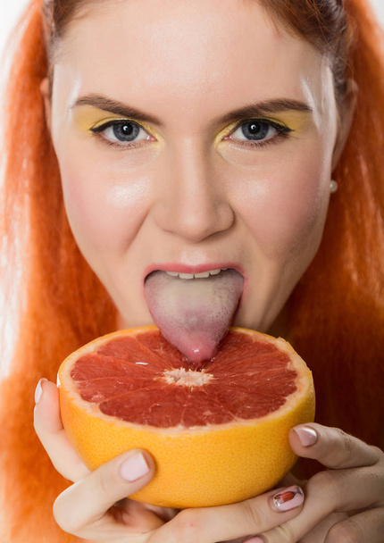Young redhead woman licks a grapefruit on a white background. concept of healthy eating - Fotó, kép