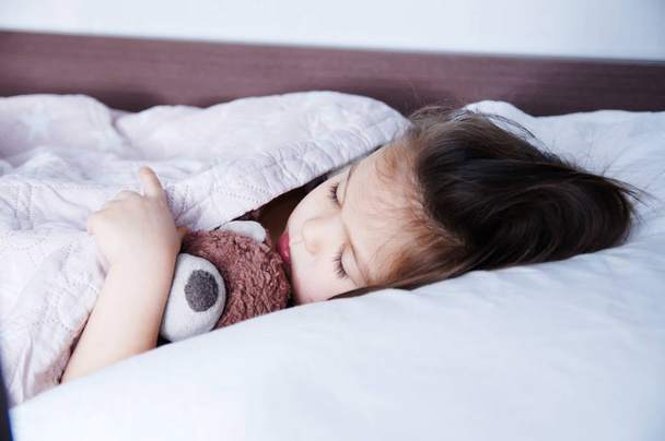 Pikkutytöt nukkuvat sängyllä. nukkumisaikataulu kotimaisessa elämäntavassa. söpö vauva lapsi karhun kanssa
 - Valokuva, kuva
