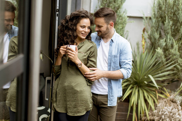 Feliz joven linda pareja enamorada abrazándose y bebiendo café en casa junto a la ventana
 - Foto, Imagen