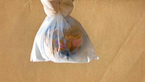 a teenage girl holds a plastic bag in her hand that contains a mini globe, recycled paper background, footage suitable for telling about problems of ecology and respect for nature and the world - Imágenes, Vídeo