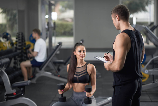 Energetic girl and man in black talking in gym. - Фото, изображение