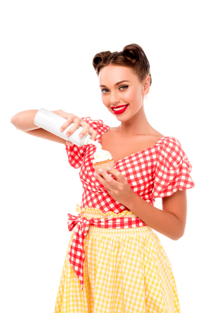 Beautiful pin up girl applying whipped cream on cupcake isolated on white - Photo, Image