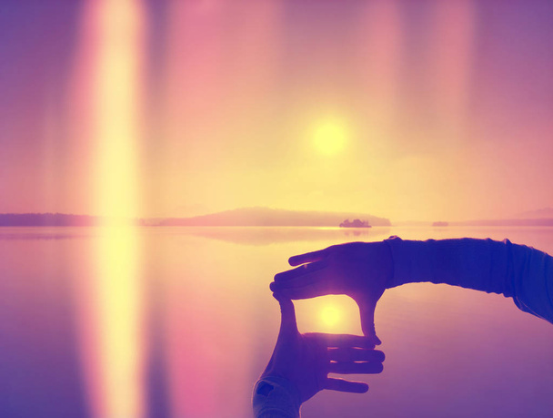 Resumen, sobre filtrado. Las manos crean un marco divertido con puesta de sol inmerso en el horizonte. Tarde de otoño en el lago
. - Foto, Imagen