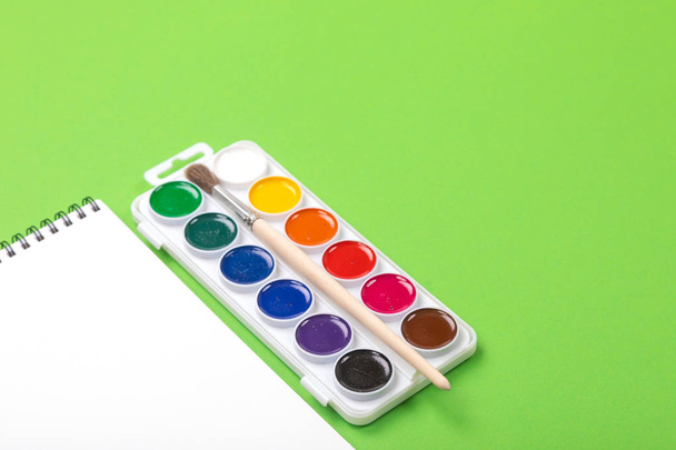 Акварельные краски и кисти с альбомом для рисования на зеленом фоне
 - Фото, изображение