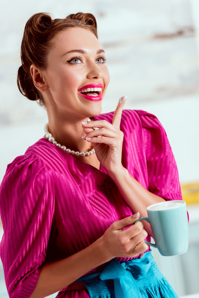 Stílusos pin-up lány vörös ruha és a gazdaság a kávéscsésze kék kötény - Fotó, kép