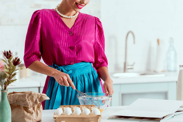 Osittainen näkymä melko pin up tyttö sekoittamalla leivonnaiset ainekset seisovat keittiön pöydän ääressä
  - Valokuva, kuva