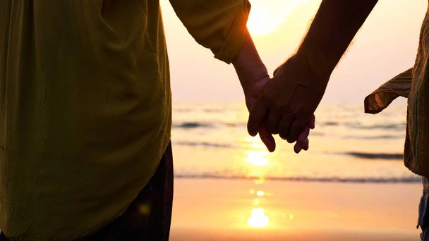 Крупным планом руки пожилой пары, стоящей на пляже и любующейся закатом
. - Фото, изображение