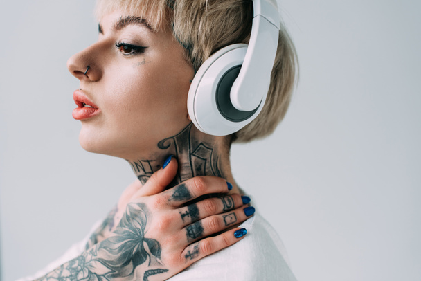 rubia mujer tatuada escuchando música en auriculares aislados en gris
  - Foto, imagen