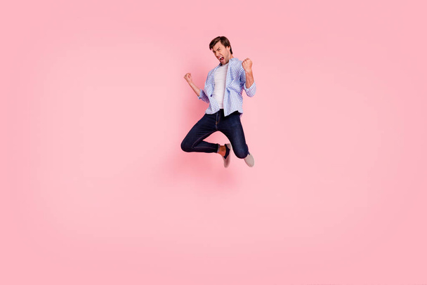 Full length body size photo of jumping high crazy cheer he his him handsome glad sad unhappy yelling loudly arms raised wearing casual jeans denimcheckered plaid shirt isolated on rose background - Photo, Image