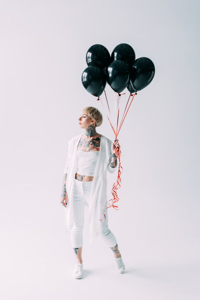 attractive blonde girl with tattoos holding black balloons on grey background  - 写真・画像