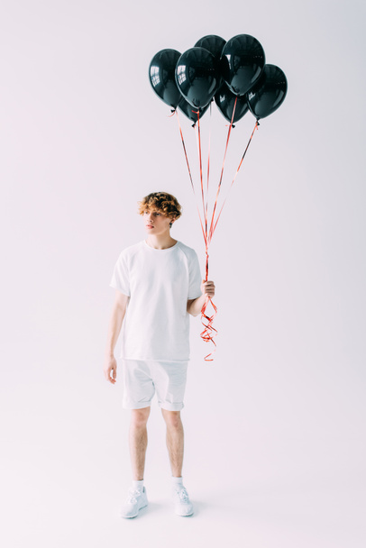handsome man with curly hair holding black balloons on grey background  - Foto, immagini