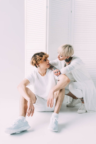 blonde girl and handsome boyfriend looking at each other and sitting on grey background - Foto, Imagem