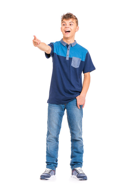 Full length portrait of young caucasian teen boy isolated on white background. Funny teenager pointing finger. Handsome child looking away and laughing. - Foto, afbeelding