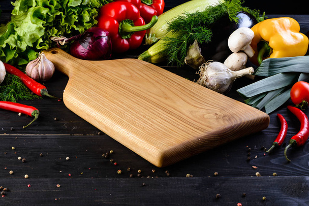 empty wooden board mockup and fresh vegetables on wooden black background - Foto, afbeelding