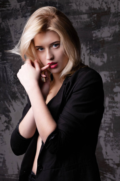 Hermosa mujer rubia con chaqueta negra posando en el estudio con sombras
 - Foto, imagen