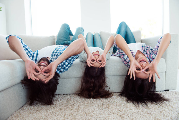 Upside down portrait of nice cool careless attractive cheerful cheery foolish crazy people mom dad lying on divan having fun in light white modern interior indoors - Foto, afbeelding