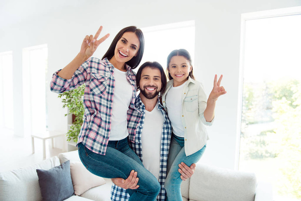 Portrait of nice cute adorable charming lovely attractive cheerful cheery spouses daddy carrying two people pre-teen girl wife having fun showing v-sign rejoice in modern white light interior room - Фото, изображение