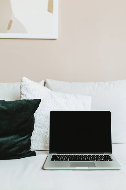 Luminoso espacio de trabajo de escritorio de oficina en casa con ordenador portátil de pantalla maqueta. Concepto de diseño interior minimalista nórdico moderno. Ordenador en la cama con almohadas
. - Foto, Imagen