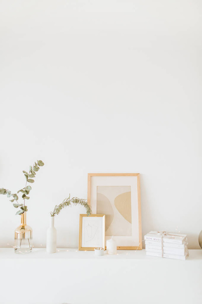 Styled Interior Design Komposition. Fotorahmen, Eukalyptuszweig, Vase auf weißem Tisch. trendiges skandinavisches Wohnzimmer. - Foto, Bild
