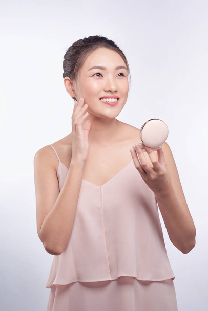 Joven asiática haciendo maquillaje, aplicando colorete a su mejilla
 - Foto, imagen