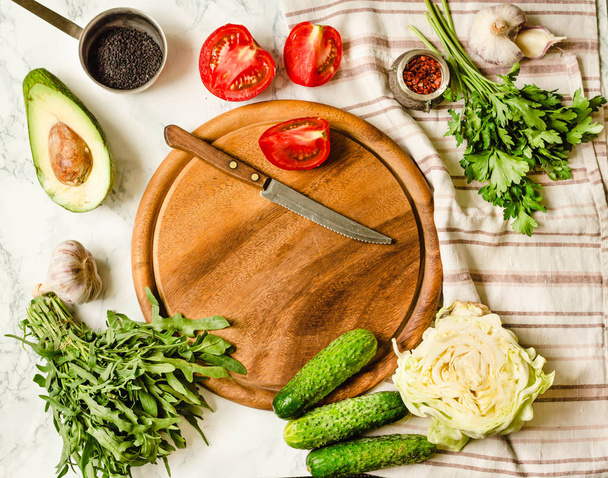 Greens, tomatoes, cucumbers, spices, avocados, vegetables, spring fresh food. Preparing raw salad. Wooden board, top view, place for text. - 写真・画像