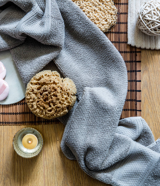 zen bath with candle and fresh towel for shower, natural sponge for cleaning, loofah for exfoliation over wooden background, top view - 写真・画像