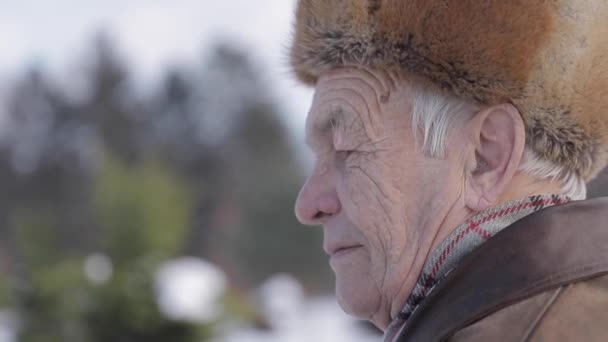 Closeup ηλικιωμένος στο χειμερινό καπέλο. Παλιά ο άνθρωπος έχει misthins στο πρόσωπο. Ευτυχισμένο παππού - Πλάνα, βίντεο