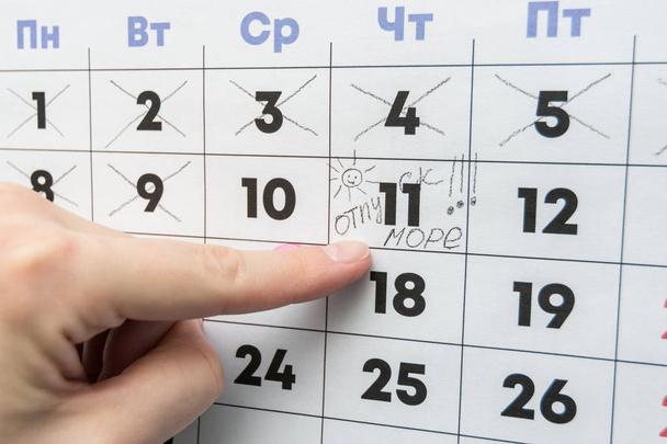 Το χέρι δείχνει την ημέρα στο ημερολόγιο με την επιγραφή διακοπές - Φωτογραφία, εικόνα