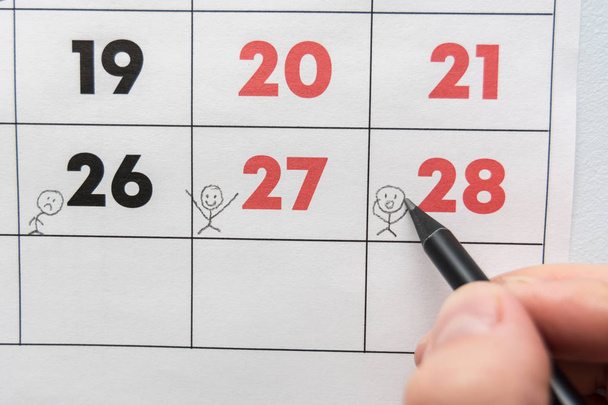 A pencil draws funny people on a sheet of a wall calendar - 写真・画像